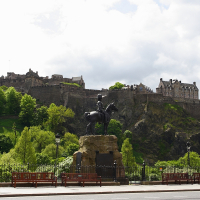 A statue of a mounted figure dominates the foreground, encapsulating Scotland's rich culture, with the majestic Edinburgh Castle perched atop a rocky crag in the distance, all set against a partly cloudy sky