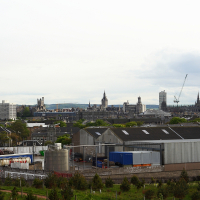 An overcast cityscape view featuring industrial buildings in the foreground with historical architecture and modern skyscrapers in the background, under a cloudy sky, epitomizes Scotland's diverse appeal to tourism and travel