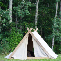 A small, white canvas tent is set up on a grassy area, with dense green trees in the background. The tent has a wooden frame with decorative carvings at the top, and its entrance is open. The simple, rustic setup suggests an outdoor event or perhaps Semigallian Days 2009 in a forested area.
