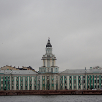 The Kunstkamera Museum, with its distinctive baroque architecture and tower, stands along the Neva River embankment on a cloudy day in St. Petersburg, Russia.