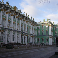 The winter palace in St. Petersburg, Russia, flaunts its ornate baroque façade with rich green and white colors, intricate gold embellishments, and grand windows, under a clear blue sky