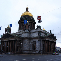 St. Isaac's Cathedral dominates the skyline with its grand dome and neoclassical architecture, as flags flutter above a dampened street in St. Petersburg, Russia.