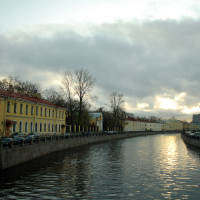 A serene dusk over a calm canal in St. Petersburg, flanked by European classical architecture under a cloud-streaked sky, reflecting the waning light.