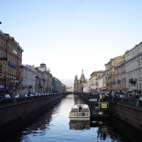 A tranquil evening settles over the St. Petersburg canal lined with historic buildings, where a single tour boat floats gently, under the gaze of a distant ornate cathedral.