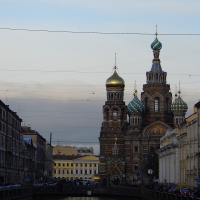 A tranquil evening view of the Griboedov Canal with the ornate Church of the Savior on Spilled Blood in the backdrop, showcasing its distinctive onion domes and intricate architecture, in St.