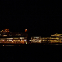Illuminated facades of grand buildings in St. Petersburg cast a stunning reflection on the dark waters of a river at night, showcasing an impressive display of architectural lighting.