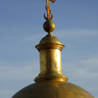 Golden dome with an orthodox cross gleaming against a clear blue sky in St. Petersburg, symbolizing religious faith and architecture.