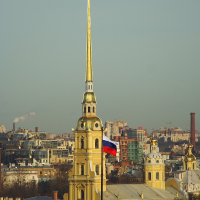 Golden spire of the Peter and Paul Cathedral, with the Russian flag fluttering below, rises above the historic skyline of St. Petersburg, a key travel destination in Russia, against a clear sky.