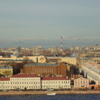 A panoramic view of St. Petersburg with neoclassical architecture, smokestacks in the distance emitting smoke, and a clear blue sky, showcasing urban life and industrial activity.