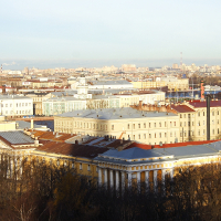 An aerial view of St. Petersburg, a historic cityscape with classical architecture, featuring sprawling buildings with colorful roofs under a clear blue sky, highlighting the grandeur of an old European city.
