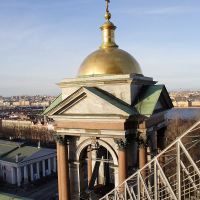 An architectural dome with a golden spire sits atop a classical building, bathed in soft sunlight, with a sweeping view of St. Petersburg stretching into the horizon under a clear blue sky.