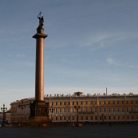 The Alexander Column towers over Palace Square in St. Petersburg at dusk, with a bronze angel holding a cross at its peak and the General Staff Building stretching in the background under a clear sky.