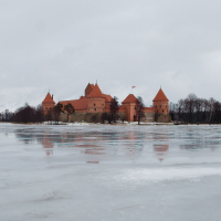 A Trakai medieval castle reflected on the icy surface of a tranquil lake under overcast skies, exhibiting a serene winter landscape.