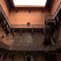 An ancient brick fortress courtyard of Trakai Castle in Lithuania, with weathered wooden staircases leading upwards, remnants of snow at the base, under a gray, overcast sky.