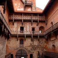 A Trakai medieval brick castle courtyard with wooden balconies, staircases, and an arched gateway, exhibiting the robust architecture and fortifications typical of Lithuania's historical military structures.