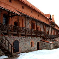 A medieval red brick castle with wooden staircases and snow partially covering the ground, evoking a historic atmosphere on a cloudy day near Trakai.