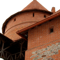 A medieval red brick tower with a conical roof, part of the old Trakai Castle, stands under a hazy sky, illustrating historical architecture and heritage in Lithuania.