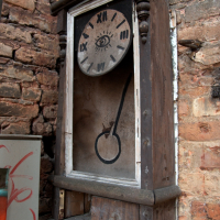 An antique clock with roman numerals displayed within a weathered wooden frame against a brick wall in Vilnius, its hands at a standstill, marking the passage of forgotten time.