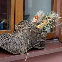 A rustic wicker shoe serves as a charming planter containing a variety of dried flowers and grasses in Vilnius, adorning a windowsill and adding a touch of whimsy to the outdoor