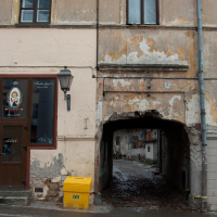 A weathered facade with peeling paint overlooks a cobblestone street, leading to an arched tunnel in the historic Vilnius neighborhood.