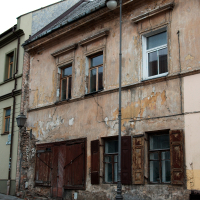 An old, weathered building with peeling plaster and boarded-up windows stands deserted on a cobblestone street in Vilnius, under the watch of a single streetlamp.