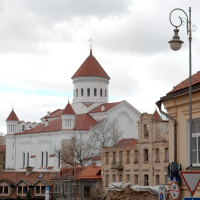 A weathered urban scene in Vilnius with diverse architectural styles, featuring graffiti-covered barriers, a vintage street lamp, and in the background, an imposing building with a prominent white tower and red roof