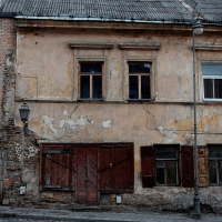 An aging building in Vilnius, with weathered facade and peeling paint, stands neglected, its windows boarded up and entrance gated, evoking a history lost to time on a deserted street.