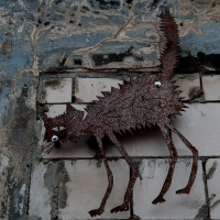 A rust-colored metal sculpture of a fantastical creature with sharp features clings to a weathered wall in Vilnius, merging industrial art with urban decay.