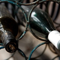 Dusty wine bottles lie horizontally in an iron rack in Vilnius, suggesting a collection with potential vintage value or a long-forgotten corner of a cellar.