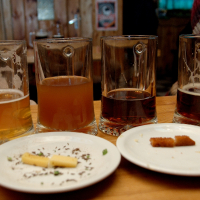 A variety of half-consumed beers in glasses with two plates containing leftover appetizers, suggesting a casual gathering at a rustic bar or pub in Vilnius.