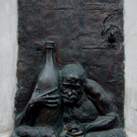 A bronze bas-relief sculpture in Vilnius depicts a contemplative figure with a long beard, clutching a bottle and resting against a wall, blending art with the urban fabric.