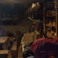 A dimly lit rustic workshop in Vilnius with pottery pieces on shelves, a wooden bench, and assorted fabrics draped over objects, exuding an air of creative chaos and traditional craft.