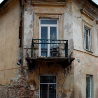 An old, weathered two-story building in Vilnius, with peeling paint and a rusty balcony, displaying signs of neglect and the passage of time.