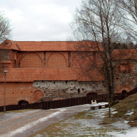 A historic red-brick building with arches, possibly an old fortress or monastery, sits atop a hill in Vilnius, its aged walls contrasting against a dusting of snow, with bare trees