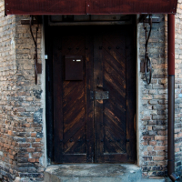 An aged wooden door with iron hinges, flanked by brick walls under a tiled canopy in Vilnius, exuding rustic charm and a sense of history.