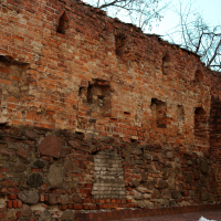 An aged brick wall in Vilnius, with signs of deterioration and patchwork, hinting at historical significance, stands tall against the remnants of snow, suggesting a timeline that transcends seasons and possibly