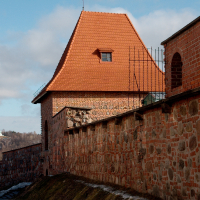 An old fortified brick building in Vilnius with a tiled roof stands under a blue sky with wispy clouds, showing the architectural heritage and the strength of historical fortifications.