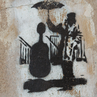 A stencil graffiti artwork on a wall in Vilnius, depicting a silhouette of a musician, possibly a street performer, playing a guitar under an umbrella with an urban backdrop.