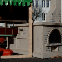 A stationary carousel with vibrant colors and playful details, including a red boot and a mock fireplace, sits idle under daylight in Vilnius, evoking a sense of whimsy in an urban square.