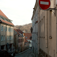 A narrow Vilnius street descends gently between historic buildings under a clear sky, with a prominently placed 'do not enter' sign signaling a one-way road.