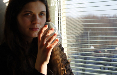 A Woman Balancing A Glass Of Water As She Sits On A Window Sill.